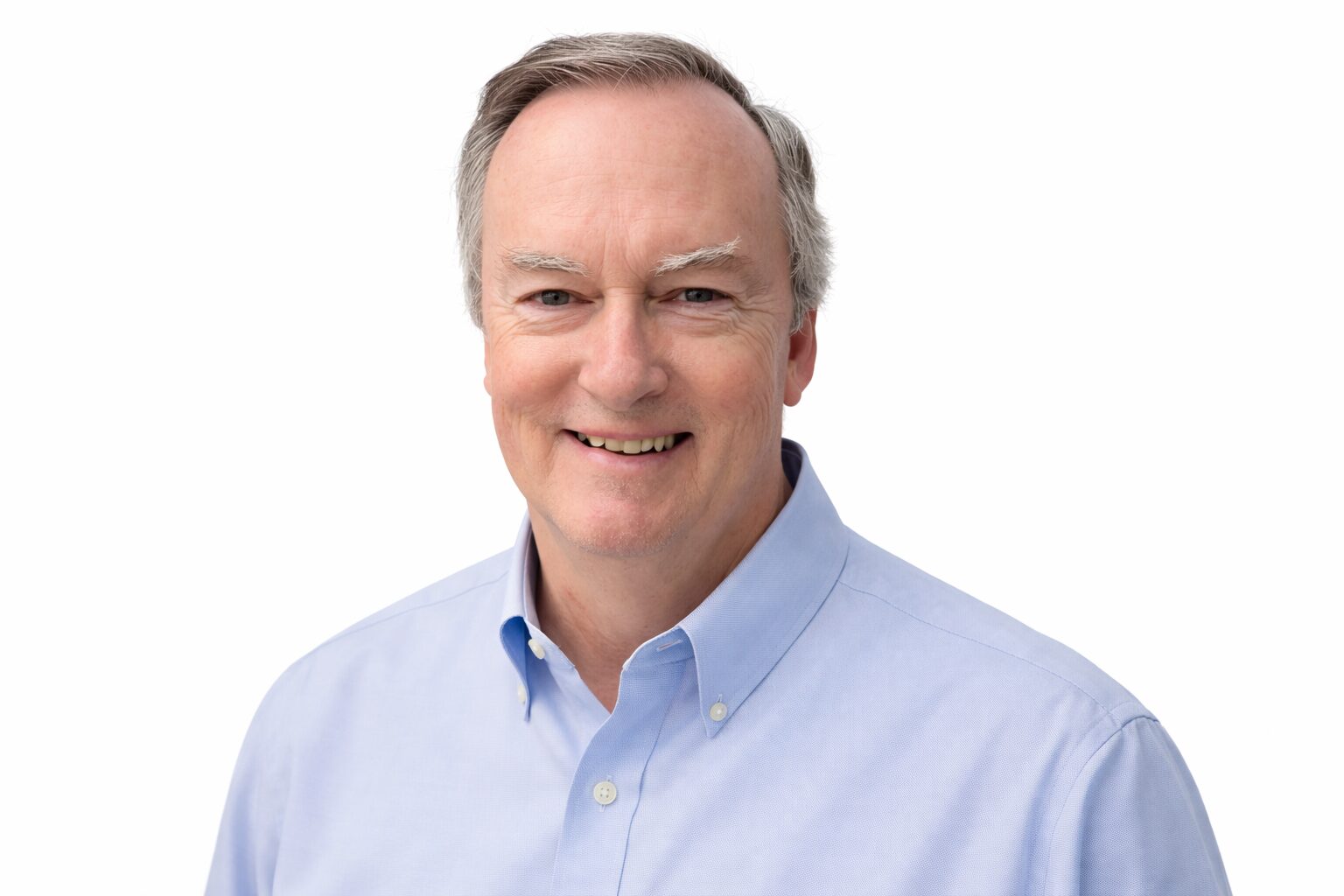 Smiling middle-aged man with gray hair wearing a light blue collared shirt, posed against a plain white background.