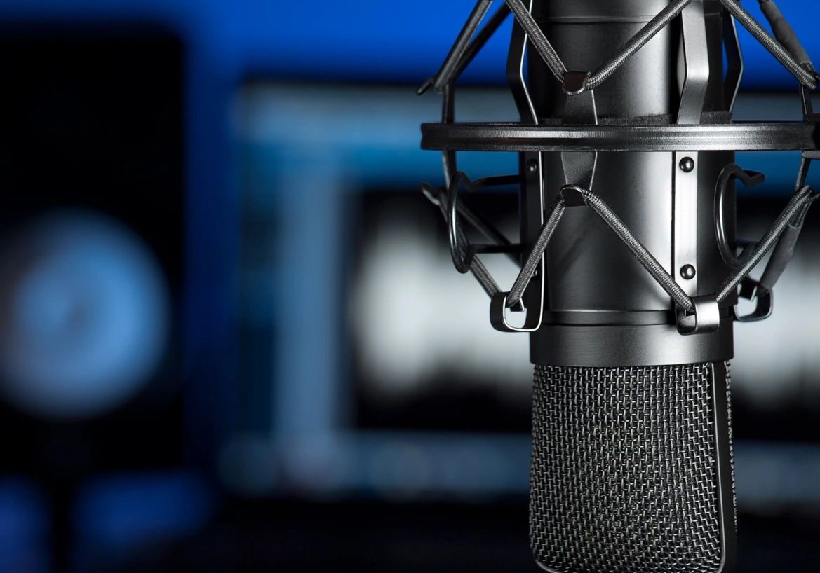 Close-up of a studio microphone with a pop filter, set against a blurred background of audio equipment and blue lighting.
